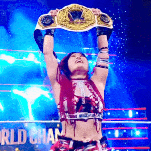 a woman in a wrestling ring is holding a world heavyweight championship belt over her head .