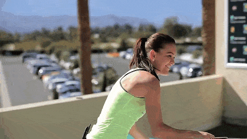 a woman in a green tank top is riding a bicycle