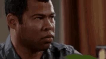 a man is sitting at a table with a book in his hand and making a funny face .