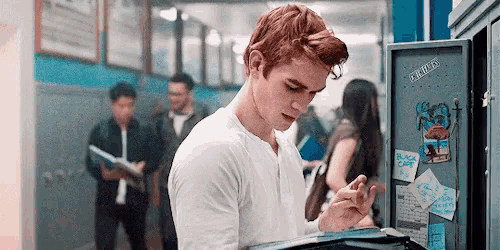 a young man with red hair is looking at his phone in a hallway .