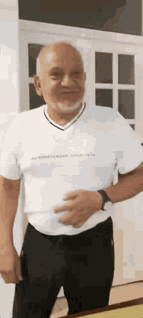 an elderly man with a beard is wearing a white shirt and black pants .