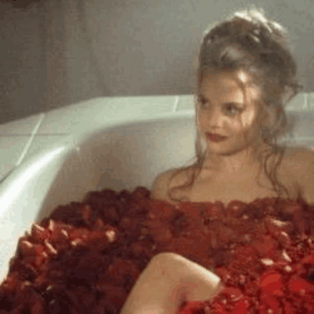 a woman is taking a bath filled with red roses .