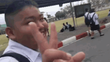 a young boy in a school uniform is making a peace sign with his hands .