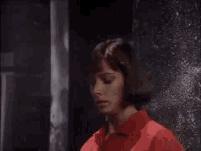 a woman in a red shirt is smoking a cigarette in front of a ghost in a dark room .