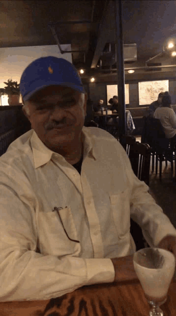 a man wearing a blue hat is sitting at a table with a drink