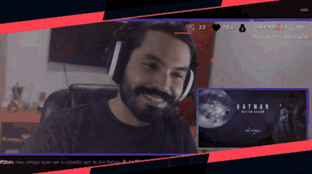 a man wearing headphones is smiling in front of a batman screen
