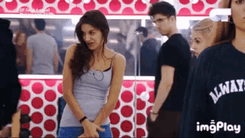 a woman wearing a gray tank top and a black always shirt stands in front of a group of people