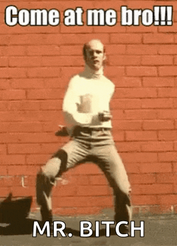 a bald man is dancing in front of a red brick wall with the caption come at me bro !!! mr. bitch
