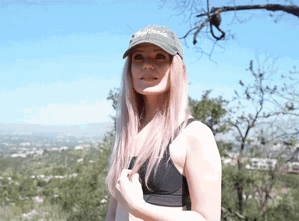 a woman wearing a california hat stands in front of a tree