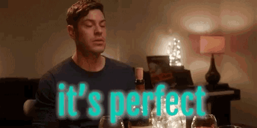 a man sits at a table with a bottle of wine and glasses and the words it 's perfect above him
