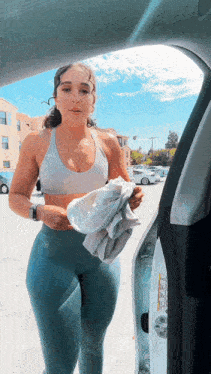 a woman in a sports bra and leggings is standing next to a car