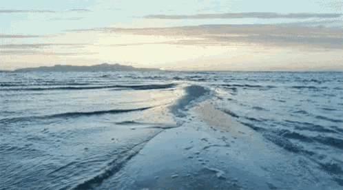 a beach with waves crashing on the sand and mountains in the distance