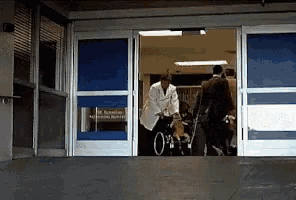 a doctor pushes a patient in a wheelchair through a hospital entrance