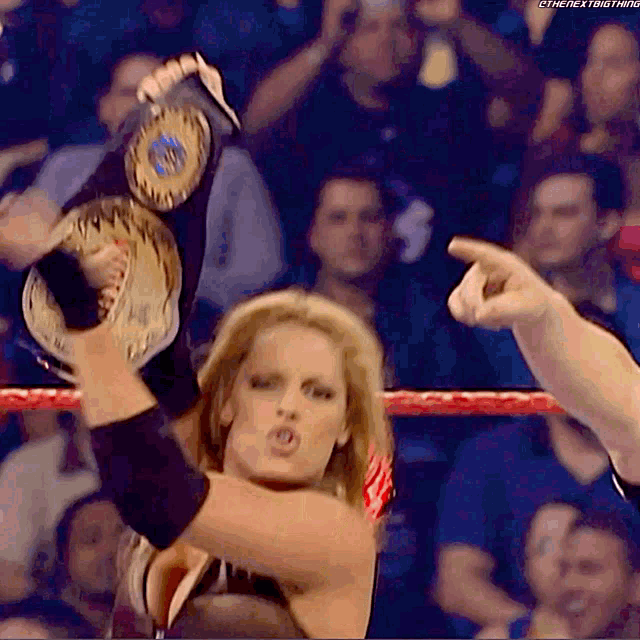 a woman in a wrestling ring is holding a world heavyweight championship belt above her head