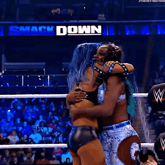 a couple of women hugging in a wrestling ring with the words smack down in the background
