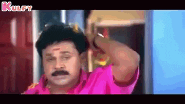 a man with a mustache and a pink shirt is standing in a room .