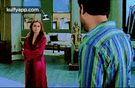 a man and a woman are standing next to each other in a living room . the woman is wearing a red robe .