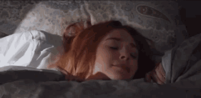 a woman is laying in bed with her eyes closed and her head on a pillow .