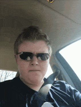 a man in a car wearing sunglasses and a seat belt