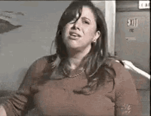 a woman in a red sweater is making a funny face while standing in front of a wall .