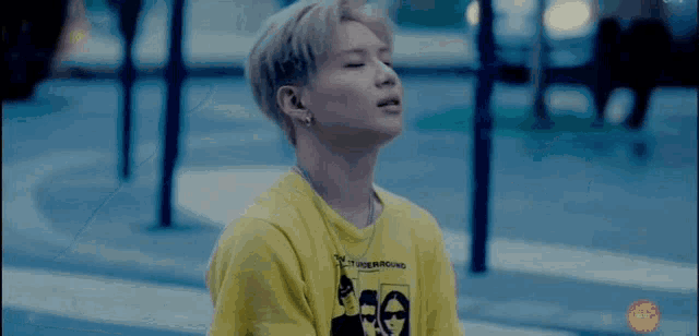 a young man wearing a yellow t-shirt and a necklace is sitting on the sidewalk with his eyes closed .