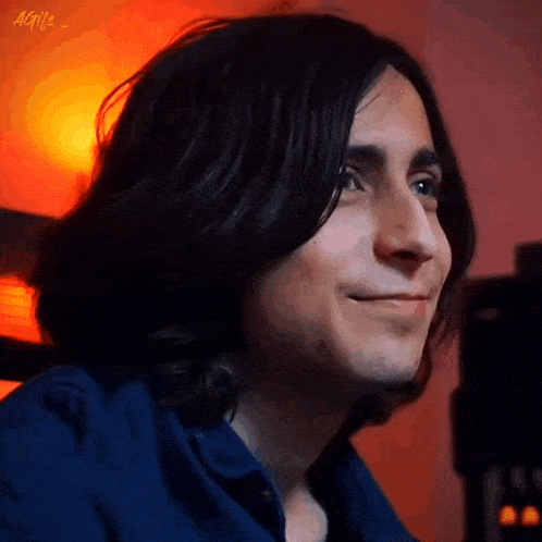 a close up of a man 's face with long hair and a blue shirt .