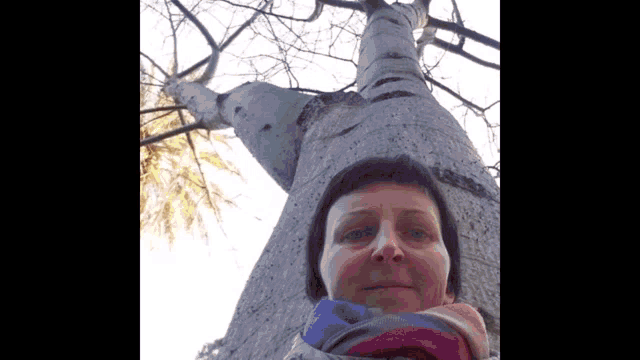 a woman is standing in front of a tree with a scarf around her neck