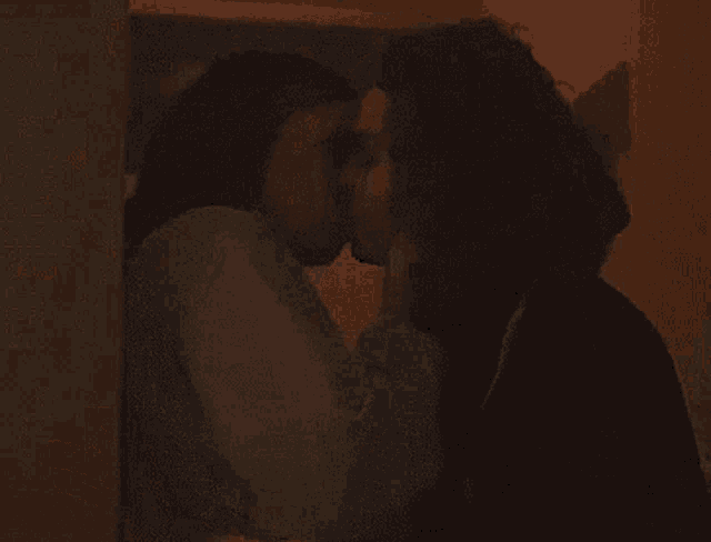 two women are kissing each other in a dark room .