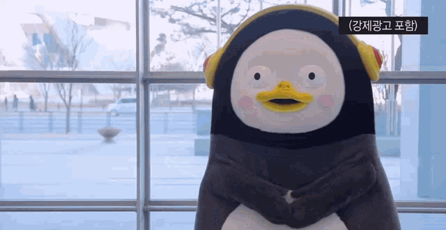 a stuffed penguin wearing headphones standing in front of a window