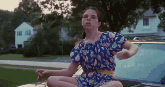 a girl in a blue dress sits on the hood of a car with her legs crossed