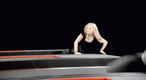 a woman is crawling on a trampoline while a person kicks her