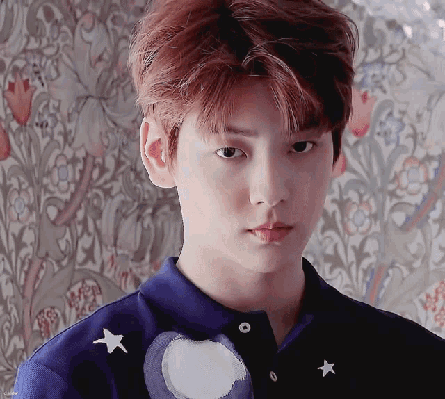 a close up of a young man 's face with a floral wallpaper behind him