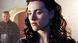 a close up of a woman 's face with a man standing in the background