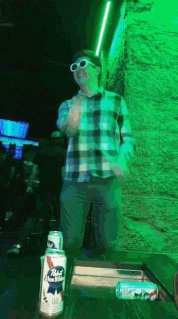 a man in a plaid shirt is dancing in front of a can of pabst blue ribbon