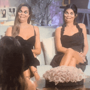 two women sitting on a couch with their legs crossed making funny faces