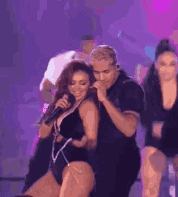 a man is singing into a microphone while a woman is dancing in front of him on a stage .