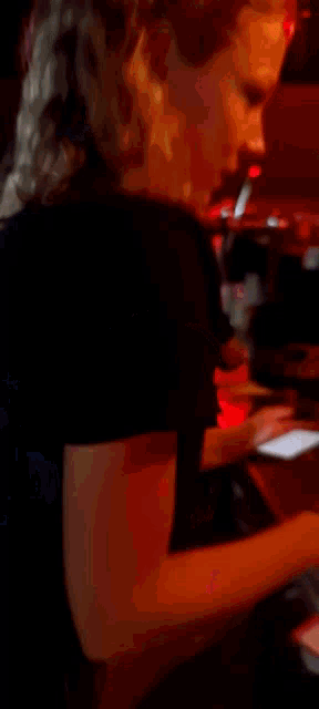 a woman with long blonde hair is standing in a dark room with a red light behind her