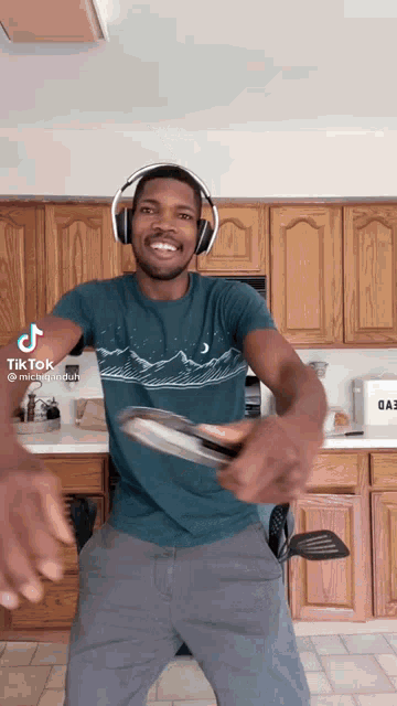 a man wearing headphones and a blue shirt with mountains on it is dancing in the kitchen