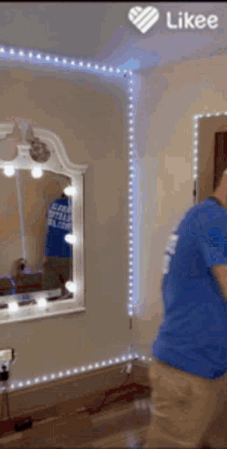 a man in a blue shirt is standing in front of a mirror with lights on the wall .