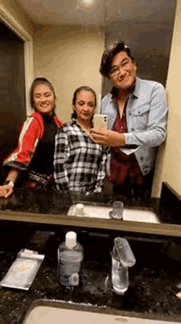 a man and two women are taking a picture of themselves in a bathroom mirror .