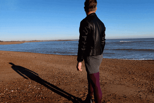 a man in a leather jacket is standing on a beach