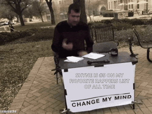 a man is sitting at a desk with a sign that says change my mind