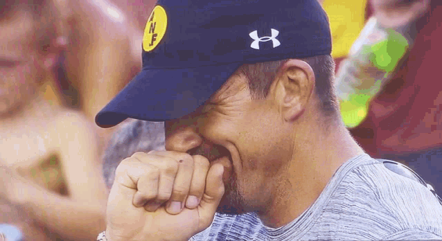 a man wearing an under armour hat covering his mouth with his fist