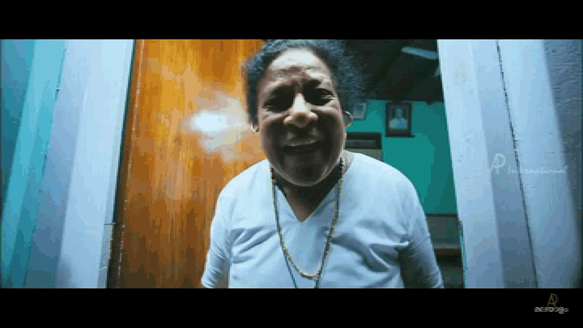 a man in a white shirt with a gold chain around his neck is standing in front of a wooden door