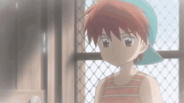 a young boy wearing a hat and a tank top is standing in front of a window .