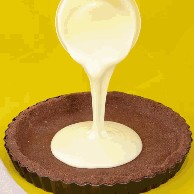 white liquid is being poured into a chocolate tart