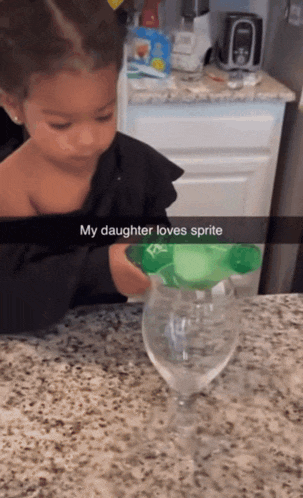 a little girl is playing with a bottle of sprite and a glass of water