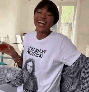 a woman is wearing a white t-shirt that says `` you know nothing '' and holding a glass of wine .