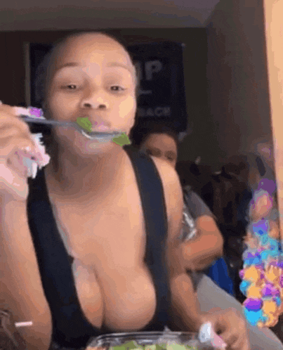 a woman in a black tank top is eating a salad with a spoon in her mouth .