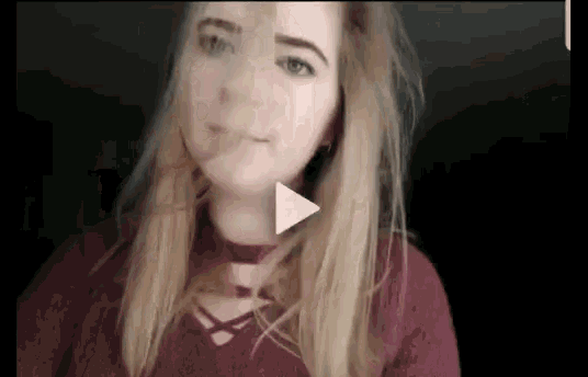 a woman in a red sweater is looking at the camera with a play button in the corner .